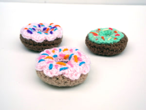 Donut-shaped catnip toys, pink with sprinkles, green with sprinkles, light brown and dark brown bases photographed on a white background 